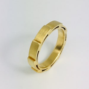 Puede incluir: Un anillo de banda de oro con un diseño geométrico único. El anillo tiene un acabado cepillado y un perfil ligeramente redondeado.