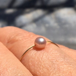 May include: A delicate gold ring with a single, light pink pearl.
