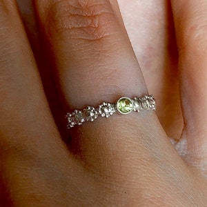 Könnte beinhalten: Ein silberner Ring mit einem grünen Edelstein in der Mitte. Der Ring ist mit kleinen, erhabenen Details verziert, die an Blumen erinnern.