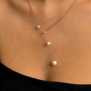 Op de afbeelding: Een delicate gelaagde ketting met drie witte parels die aan een dunne bruine koord hangen.