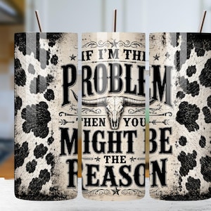 Może przedstawiać: Cylindryczny kubek z czarno-białym wzorem w łaty krowie po bokach oraz centralną grafiką czaszki byka. Tekst brzmi IF I'M THE PROBLEM THEN YOU MIGHT BE THE REASON. Projekt zawiera ozdobne gwiazdki oraz dekoracyjne zawijasy i elementy graficzne.