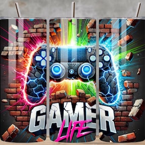 May include: A stainless steel tumbler with a vibrant design featuring a video game controller breaking through a brick wall. The design includes the words "GAMER LIFE" in bold letters, with neon blue, green, and pink accents. The tumbler has a silver straw.