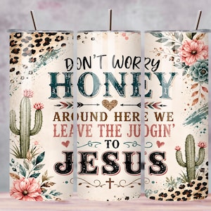 May include: A cylindrical tumbler with a metal straw featuring a cream background, leopard print accents, green cacti, and pink flowers. The text reads: DON'T WORRY HONEY AROUND HERE WE LEAVE THE JUDGIN' TO JESUS, accompanied by a glittery heart and cross.