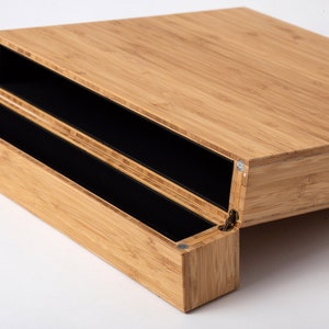 Pode incluir: Um organizador de secret&aacute;ria de bambu com tampa articulada e dois compartimentos internos pretos. O gr&atilde;o natural da madeira de bambu &eacute; vis&iacute;vel. O organizador foi concebido para guardar canetas, l&aacute;pis e outros materiais de escrit&oacute;rio.