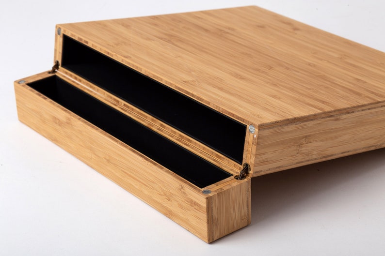 Pode incluir: Um organizador de secret&aacute;ria de bambu com tampa articulada e dois compartimentos internos pretos. O gr&atilde;o natural da madeira de bambu &eacute; vis&iacute;vel. O organizador foi concebido para guardar canetas, l&aacute;pis e outros materiais de escrit&oacute;rio.