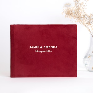 Op de afbeelding: Een rood fluwelen fotoalbum met de tekst "JAMES & AMANDA 28 augustus 2024" in wit.