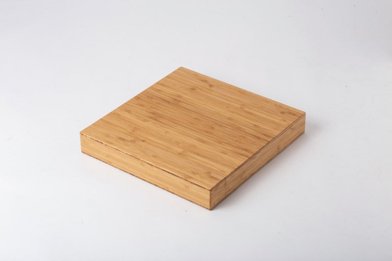 Pode incluir: Uma caixa quadrada de bambu castanho claro com tampa. A caixa &eacute; feita de v&aacute;rias tiras de bambu, criando uma superf&iacute;cie texturizada. A caixa est&aacute; em um fundo branco.