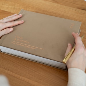 May include: A brown wedding guest book with the text "Chris & Jennifer Our Wedding Guest Book" in gold lettering.
