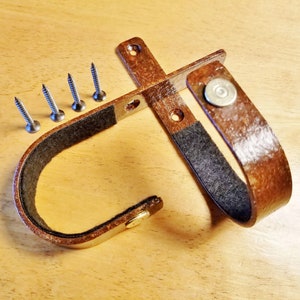 May include: A rusty brown metal wall mount with a black felt lining and a loop for hanging items. The mount is attached to a wall with screws.