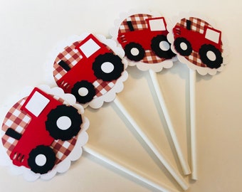 May include: Four red and black tractor cupcake toppers with white gingham backgrounds. The toppers are attached to white sticks.