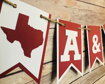 Op de afbeelding: Een rood-witte banner met de omtrek van de staat Texas, de letter A en een ampersand. De banner is aan een touwtje geregen.