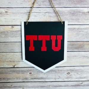 May include: A black and white pennant with a red "TTU" in the center. The pennant is hanging from a string.