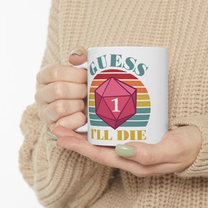 May include: White ceramic mug featuring a pink D20 die with the number 1, set against a retro sunset design. The text "GUESS I'LL DIE" is printed on the mug, making it a fun gift for gamers.