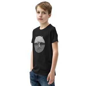 May include: Black youth t-shirt with a white graphic of a lake monster with the word "Nessie" above it.