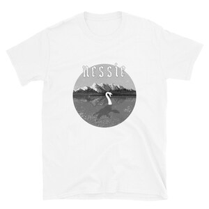 May include: White t-shirt with a black and white graphic of a lake with mountains in the background and the text "nessie" above the graphic.