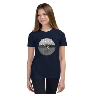 May include: A navy blue youth t-shirt with a white graphic of a lake monster with the word "nessie" above it.