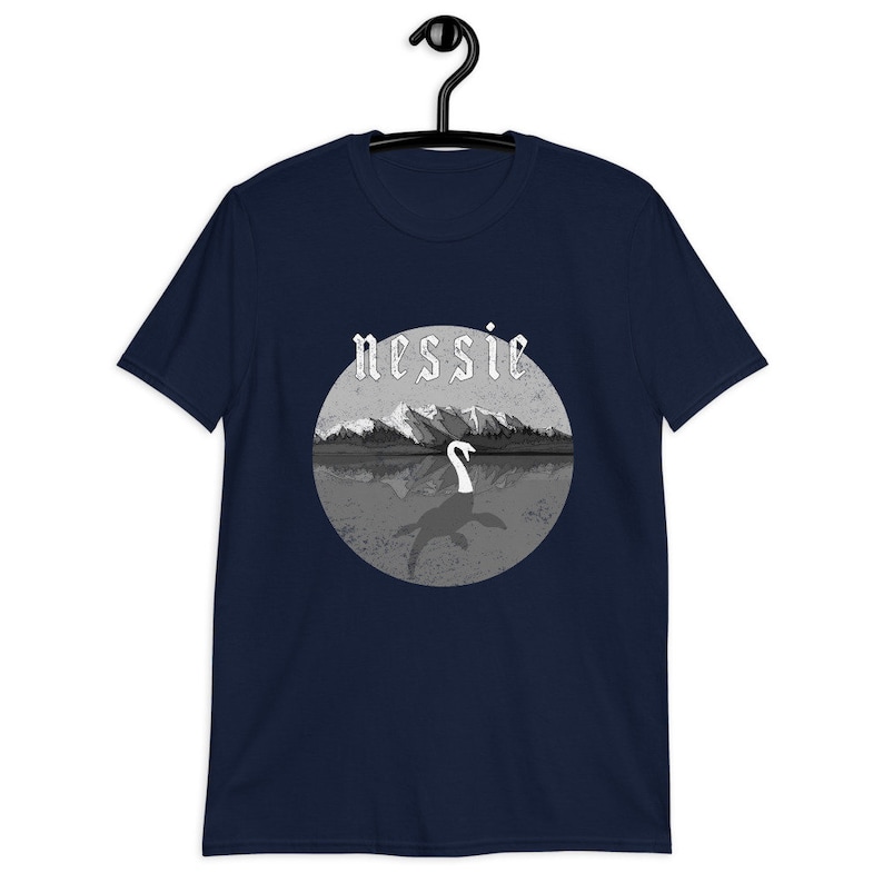 May include: A navy blue t-shirt with a graphic of a gray and white Loch Ness Monster with the word "nessie" in a gothic font above the monster.