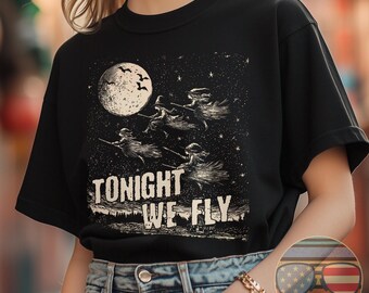May include: Black t-shirt with a graphic of witches flying on broomsticks under a full moon with the text "Tonight We Fly".