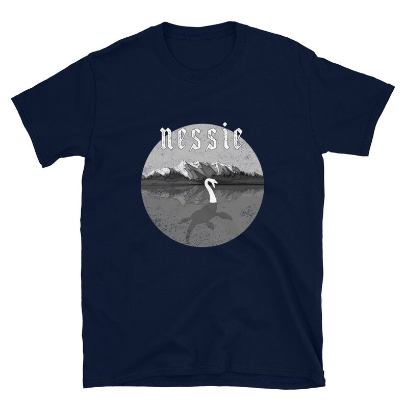 May include: A navy blue t-shirt with a graphic of a lake monster, Nessie, in a lake with mountains in the background. The text "nessie" is in a gothic font.