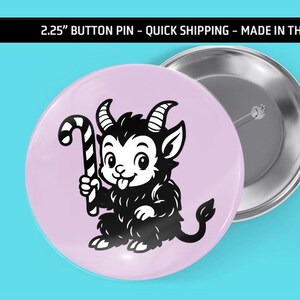 May include: A 2.25-inch button pin with a cartoon illustration of a black goat-like creature holding a candy cane on a light pink background. The pin has a silver metal back. The text "froggin happy" is also visible.