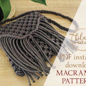 Puede incluir: Un bolso de macram&eacute; gris con flecos en la parte inferior y una correa trenzada. El bolso est&aacute; sobre una superficie de madera. El texto "PDF descarga instant&aacute;nea PATR&Oacute;N DE MACRAM&Eacute;" est&aacute; sobre un fondo blanco.