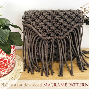 Puede incluir: Un bolso de macram&eacute; marr&oacute;n con flecos. El bolso tiene una correa y est&aacute; hecho con un cord&oacute;n grueso. El bolso est&aacute; sobre una superficie de madera con una planta en una maceta roja y blanca en el fondo. El texto "PDF instant download MACRAME PATTERN" est&aacute; en la parte inferior de la imagen.
