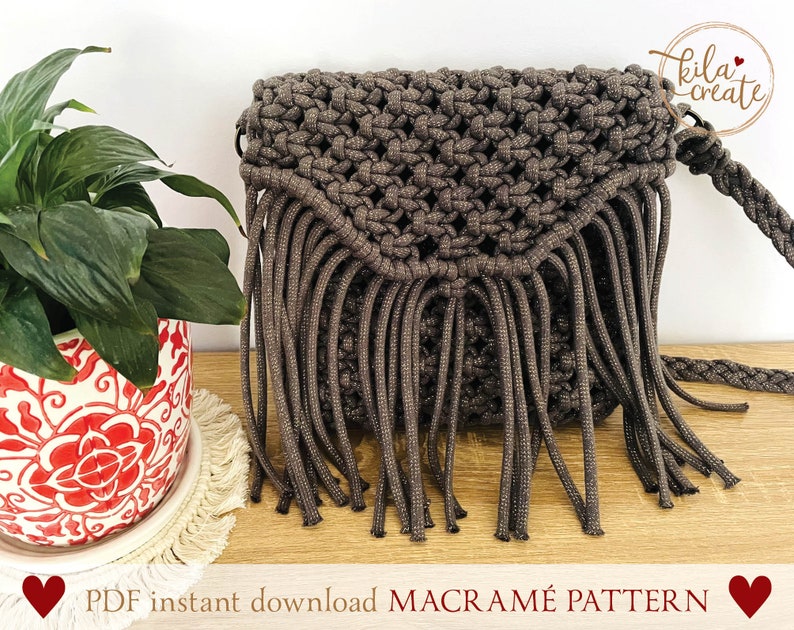 Puede incluir: Un bolso de macram&eacute; marr&oacute;n con flecos. El bolso tiene una correa y est&aacute; hecho con un cord&oacute;n grueso. El bolso est&aacute; sobre una superficie de madera con una planta en una maceta roja y blanca en el fondo. El texto "PDF instant download MACRAME PATTERN" est&aacute; en la parte inferior de la imagen.