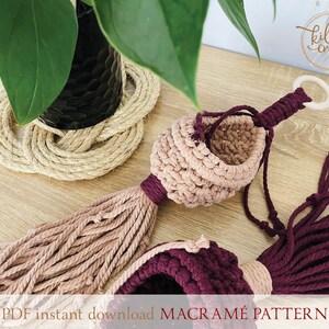 Peut inclure: Un porte-plante en macram&eacute; rose et bordeaux avec un anneau en bois en haut. Le porte-plante est fait avec un cordon de coton &eacute;pais et a un pompon en bas. Le texte "PDF instant download MACRAME PATTERN" est en bas de l'image.