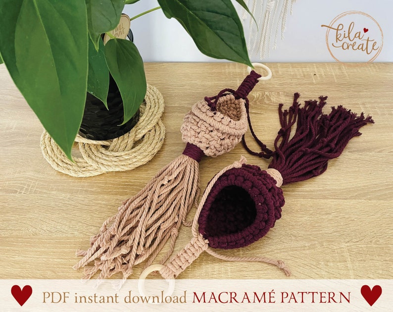 Peut inclure: Deux suspensions de plantes en macram&eacute; dans un sch&eacute;ma de couleurs rose et bordeaux. Les suspensions sont faites avec du cordon de coton et ont un pompon en bas. Les suspensions sont suspendues &agrave; une surface en bois. Le texte "PDF instant download MACRAME PATTERN" est en bas de l'image.