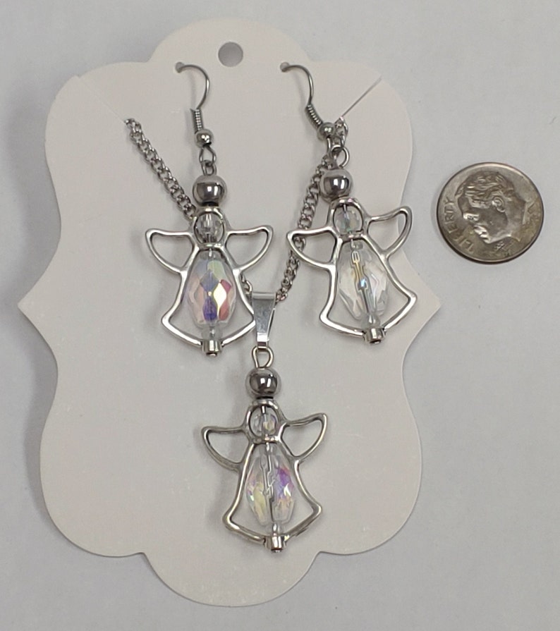 May include: A silver angel necklace and earrings set with iridescent crystal accents. The set is displayed on a white card with a silver chain and a silver angel pendant.
