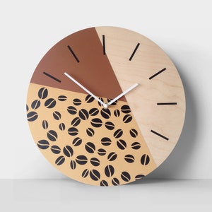 May include: A round wooden clock with a brown, beige, and natural wood finish. The clock face features a coffee bean pattern and black hour markers. The clock hands are white.