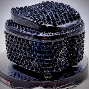 May include: A dark navy blue lidded container with a textured, spiked surface. The object features a rounded, multi-faceted exterior with numerous pointed protrusions covering both the lid and the base, creating a uniform, geometric appearance.