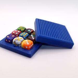May include: A collection of multi-coloured dice presented in a blue tray with a matching lid. The dice feature a variety of colours, including green, red, yellow, and orange, with white dots. The tray and lid are a solid, vibrant blue.