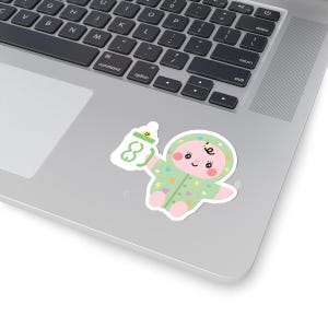 Puede incluir: Una pegatina con un bebé de dibujos animados con un mono verde sosteniendo un biberón. El bebé tiene mejillas rosadas y está rodeado de formas coloridas. El biberón tiene el número 8.