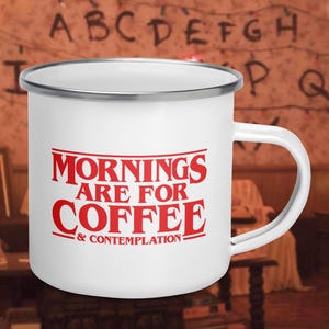 May include: White enamel coffee mug with a silver rim and handle. The mug features the text "MORNINGS ARE FOR COFFEE & CONTEMPLATION" in red, with a vintage aesthetic. The mug is designed for hot beverages.