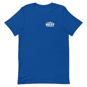 Pode incluir: Uma t-shirt de manga curta em azul royal com um gráfico branco na parte superior esquerda do peito. O texto diz THE ORIGINAL BEEF OF CHICAGOLAND numa fonte negrito sem serifa. A camisola tem um decote redondo e uma bainha reta padrão.