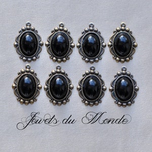 May include: Eight black oval cabochon gemstone pendants with ornate silver frames. The pendants are arranged in two rows of four. The text 'Jouets du Monde' is written in cursive at the bottom of the image.