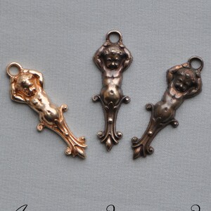 Puede incluir: Tres abalorios de querubín de metal de estilo antiguo en diferentes acabados: oro, bronce y plata. Cada abalorio presenta un querubín con los brazos levantados por encima de la cabeza y un diseño decorativo de volutas en la parte inferior.