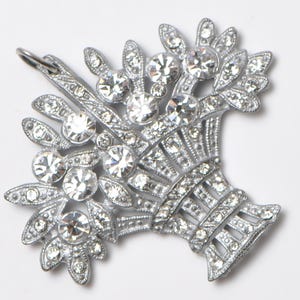 May include: A silver-toned brooch in the shape of a bouquet of flowers. The brooch is encrusted with clear, sparkling rhinestones. The bouquet is tied with a ribbon-like design at the base. The brooch has a pin clasp on the back.