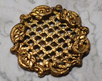 Könnte beinhalten: Ein goldfarbener, dekorativer Metallschmuck mit einem Gitterdesign und verzierten Ranken.