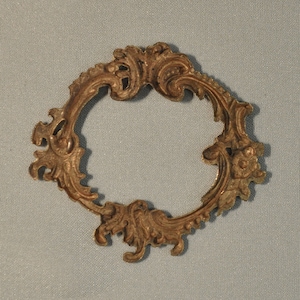 May include: A gold-toned metal frame with a decorative, ornate design. The frame is circular and has a delicate, intricate pattern.