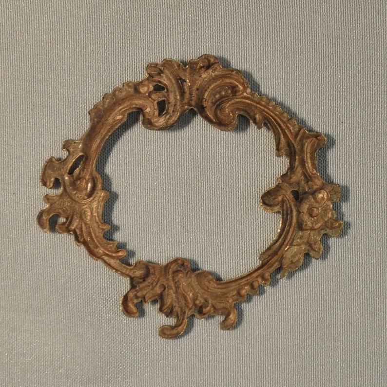 May include: A gold-toned metal frame with a decorative, ornate design. The frame is circular and has a delicate, intricate pattern.