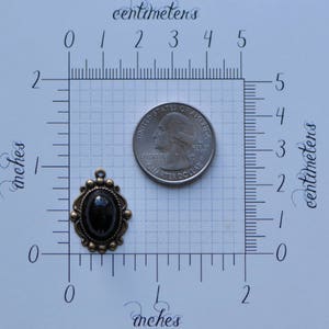 May include: A black cameo pendant with a decorative bronze frame. The pendant is about 1 inch in diameter and is shown next to a US quarter for size comparison.
