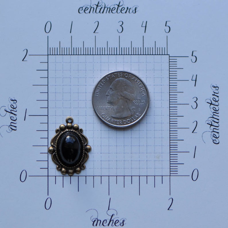 May include: A black cameo pendant with a decorative bronze frame. The pendant is about 1 inch in diameter and is shown next to a US quarter for size comparison.