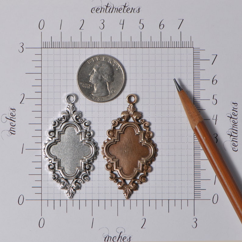 May include: Two ornate metal pendants, one silver and one copper, with a quatrefoil design. The pendants are approximately 2 inches in length and are shown next to a ruler and a US quarter for scale.