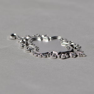 May include: A silver pendant with an ornate, intricate design. The pendant is shaped like a teardrop and has a detailed, filigree pattern.