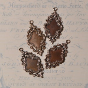 May include: Three antique-style metal charms with ornate filigree designs. Each charm features a blank, copper-colored oval in the center.