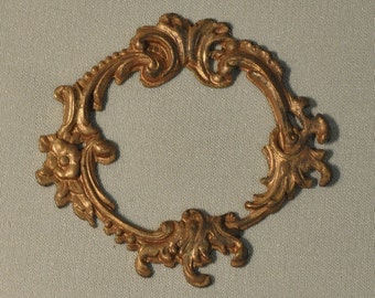Könnte beinhalten: Ein goldfarbener Metallrahmen mit einem dekorativen, verzierten Design. Der Rahmen ist oval und hat eine glatte, polierte Oberfläche.