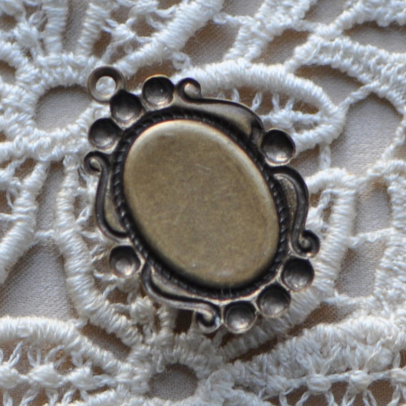 May include: A bronze-colored metal frame with an oval opening, perfect for adding a cameo or other decorative element. The frame has a decorative design with a series of small, raised circles around the edge.