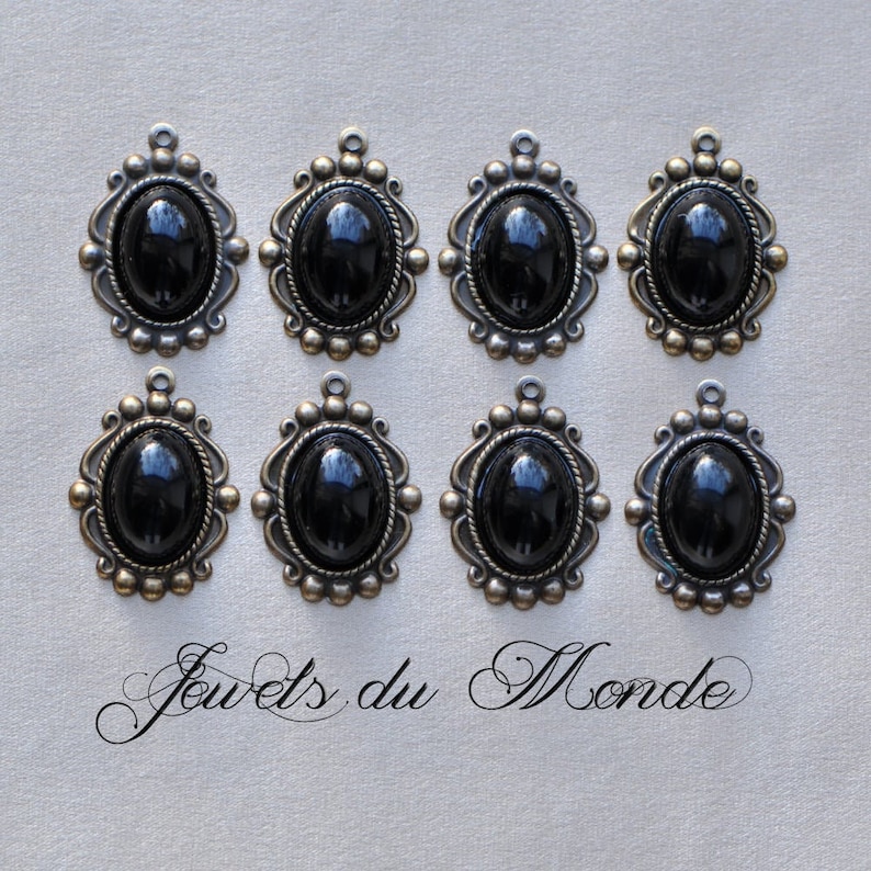 May include: Eight black oval cabochon gemstone pendants with ornate silver frames. The pendants are arranged in two rows of four. The text 'Jouets du Monde' is written in cursive at the bottom of the image.